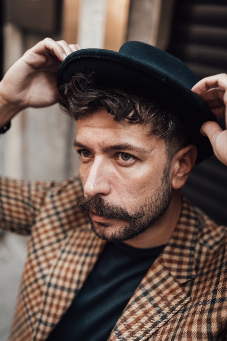 Serious Stylish Man Putting On Hat On Street