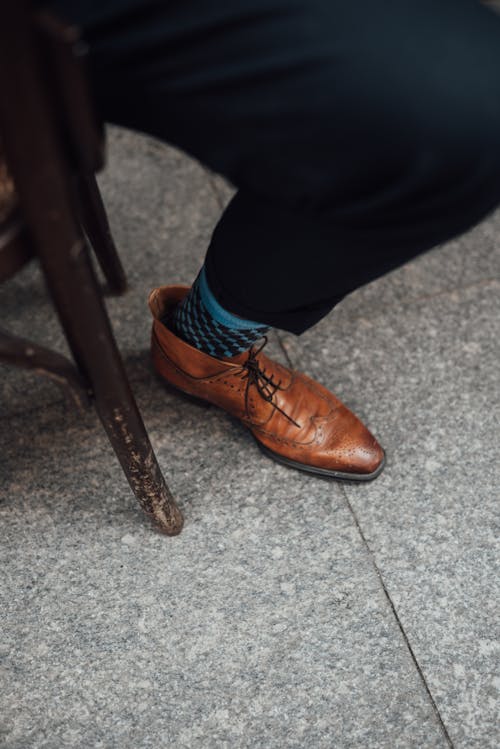 High angle crop anonymous male in elegant pants and leather shoes sitting on wooden chair