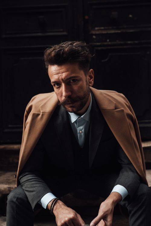 Free Confident man with mustache and beard in classy suit and jacket sitting on stairs against black door and looking at camera in daylight Stock Photo