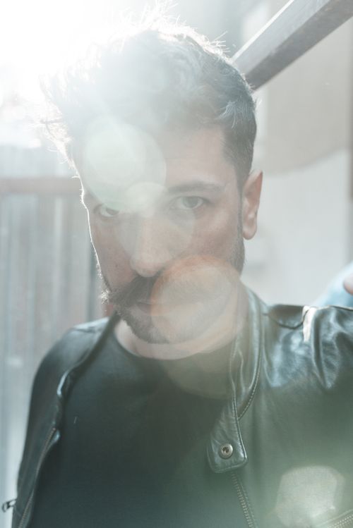 Free Confident man with beard and mustache in black leather jacket standing on street and looking at camera in sunny day Stock Photo