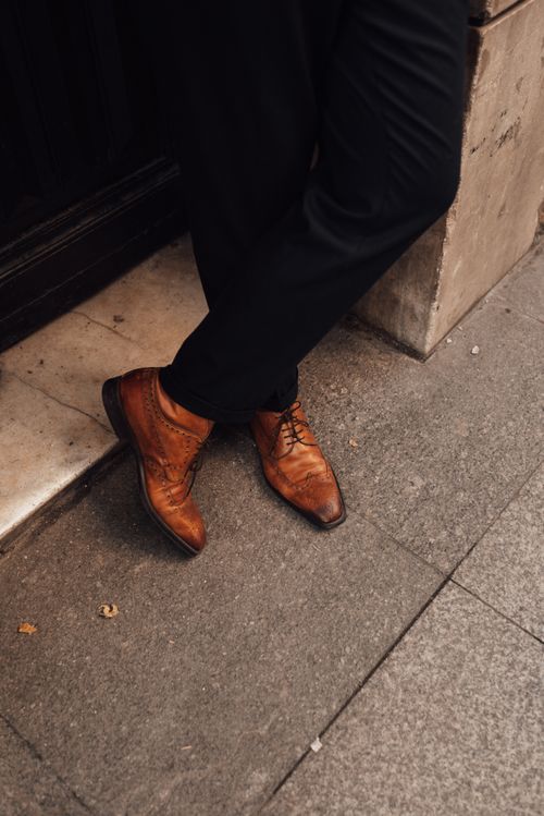 Free Crop unrecognizable male in elegant shoes and pants standing on pavement with crossed legs Stock Photo