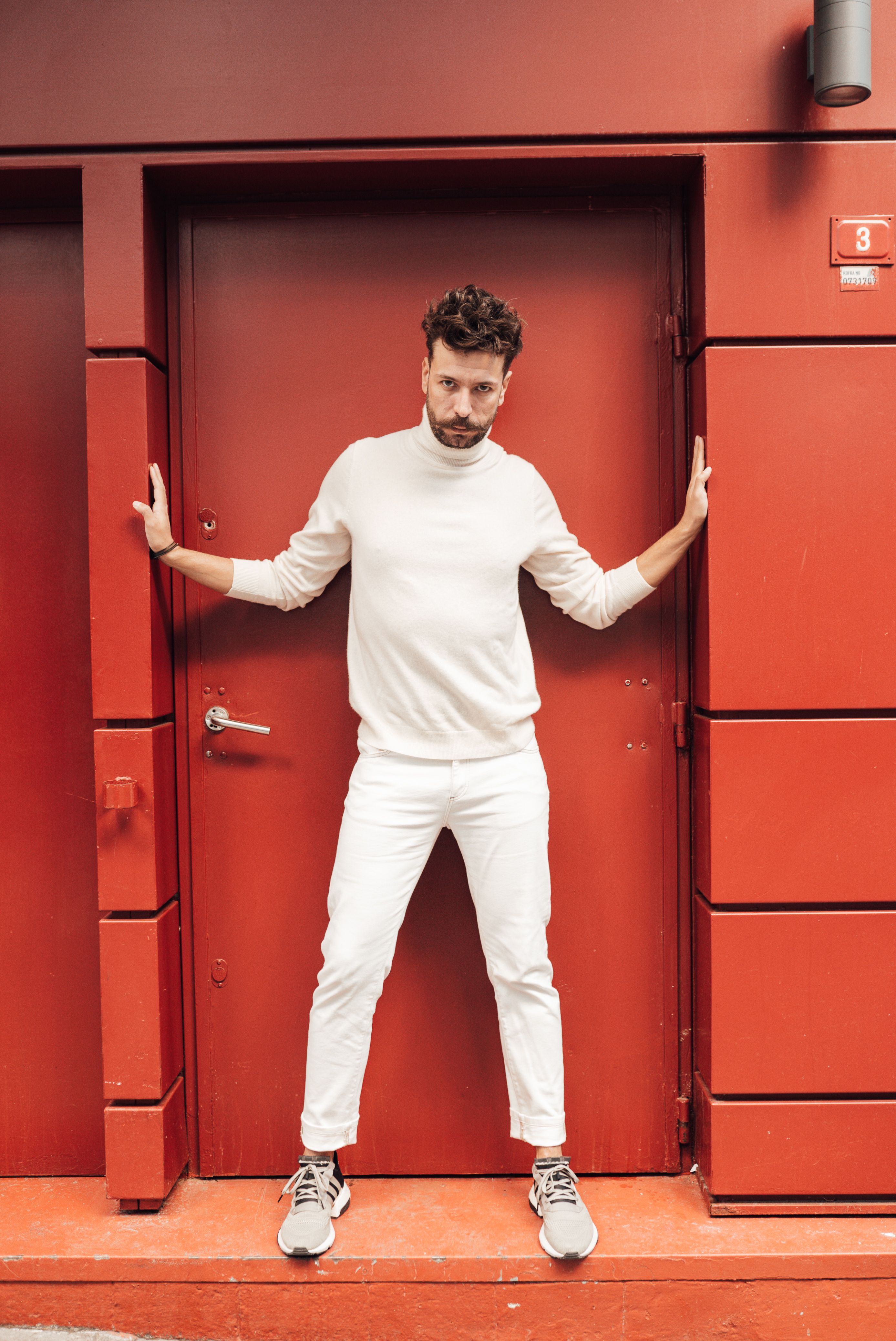 Full body of confident male model in stylish white clothes spreading arms and looking at camera