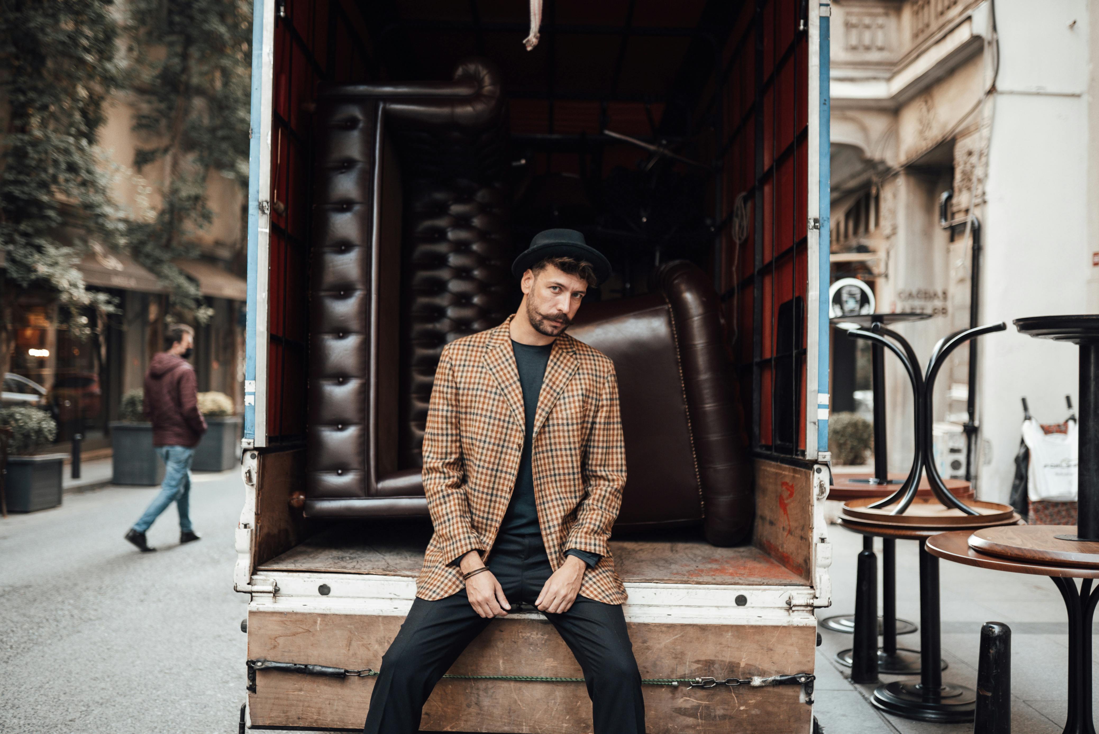 stylish man sitting in back of shabby truck with couches in street