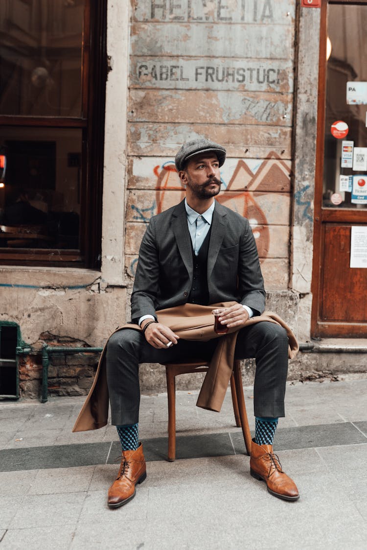 Serious Man In Formal Clothes Sitting On Chair On City Street