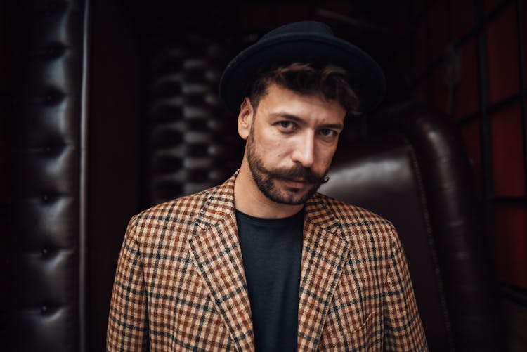 Stylish Man In Black Hat Standing Against Leather Wall