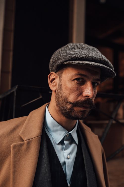 Free Confident man with beard and mustache in stylish formal outfit and cap looking at camera against building in daytime Stock Photo
