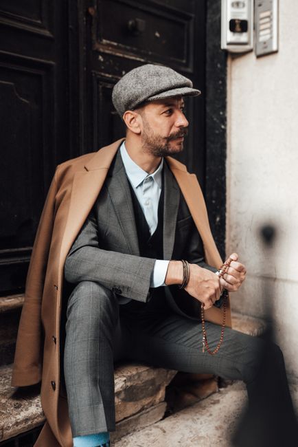 Charismatic man in stylish formal clothes sitting on stairs of building on city street and pensively looking away in daytime