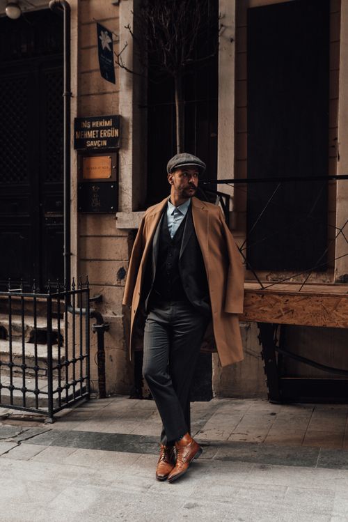 Free Full length of confident man with beard and mustache in formal clothes standing with crossed legs on street against building and thoughtfully looking away in daytime Stock Photo