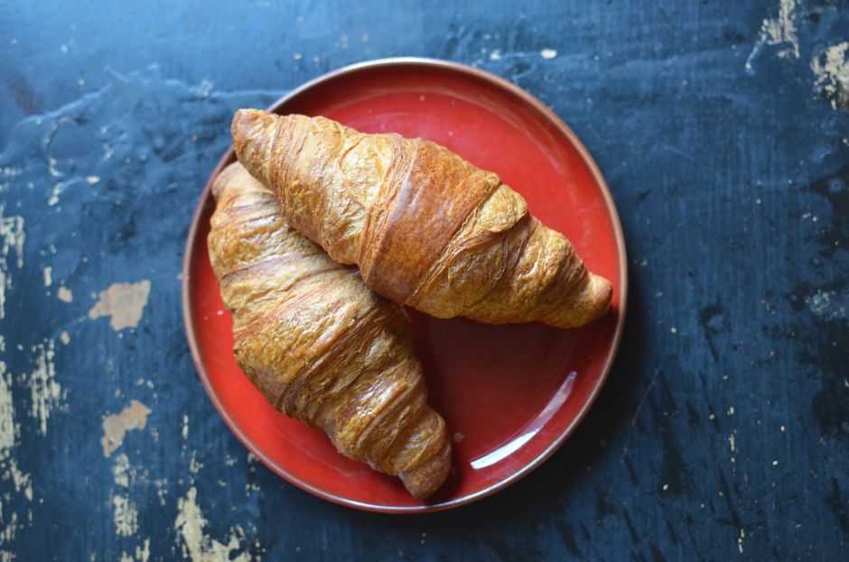 Top view of tasty sweet croissants served on red plate on shabby wooden surface of table