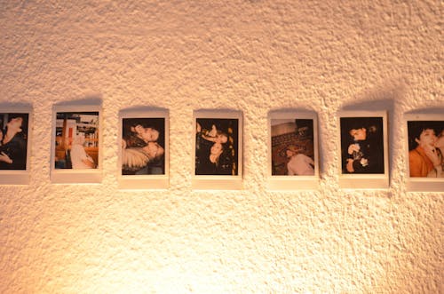 Set of colorful instant printed pictures placed on texture white wall in dark room illuminated with nightlight