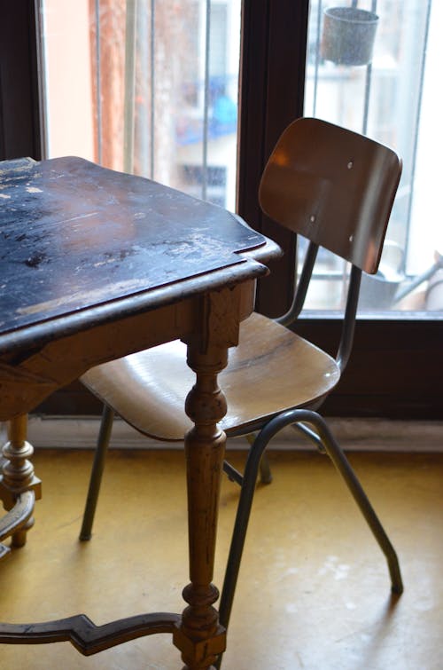 From above of aged shabby wooden table and chair placed near balcony door in room