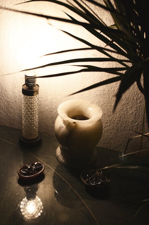 From above of retro lamp illuminating dark room placed on table near empty vase and green plant