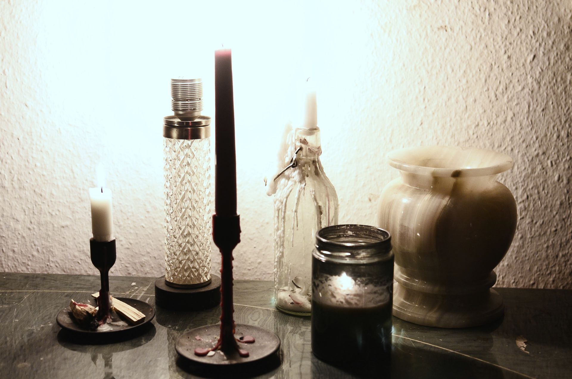 Glowing lamp illuminating dark room placed on table near burning candles on candlesticks and empty ceramic vase