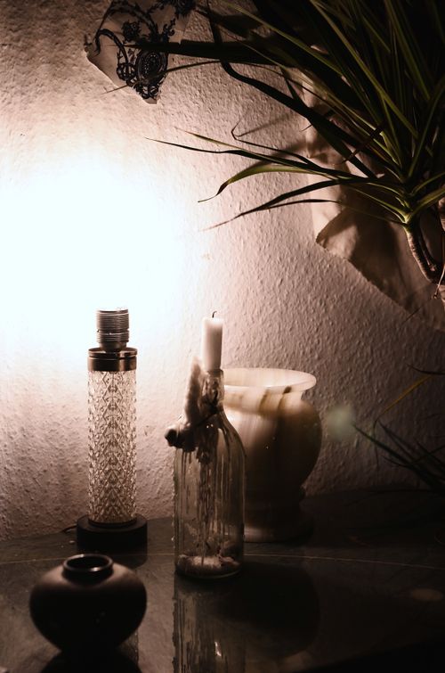 Free Glowing retro lamp illuminating dark room placed on table near empty ceramic vase and candle in glass bottle and green plant Stock Photo