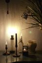 Table with burning candles on candlesticks and glowing lamp near empty ceramic vase and green plant in dark room