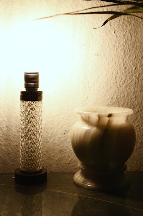 Free Interior of room with vintage glass lamp placed on table with white onyx vase near plant with green leaves and white wall Stock Photo