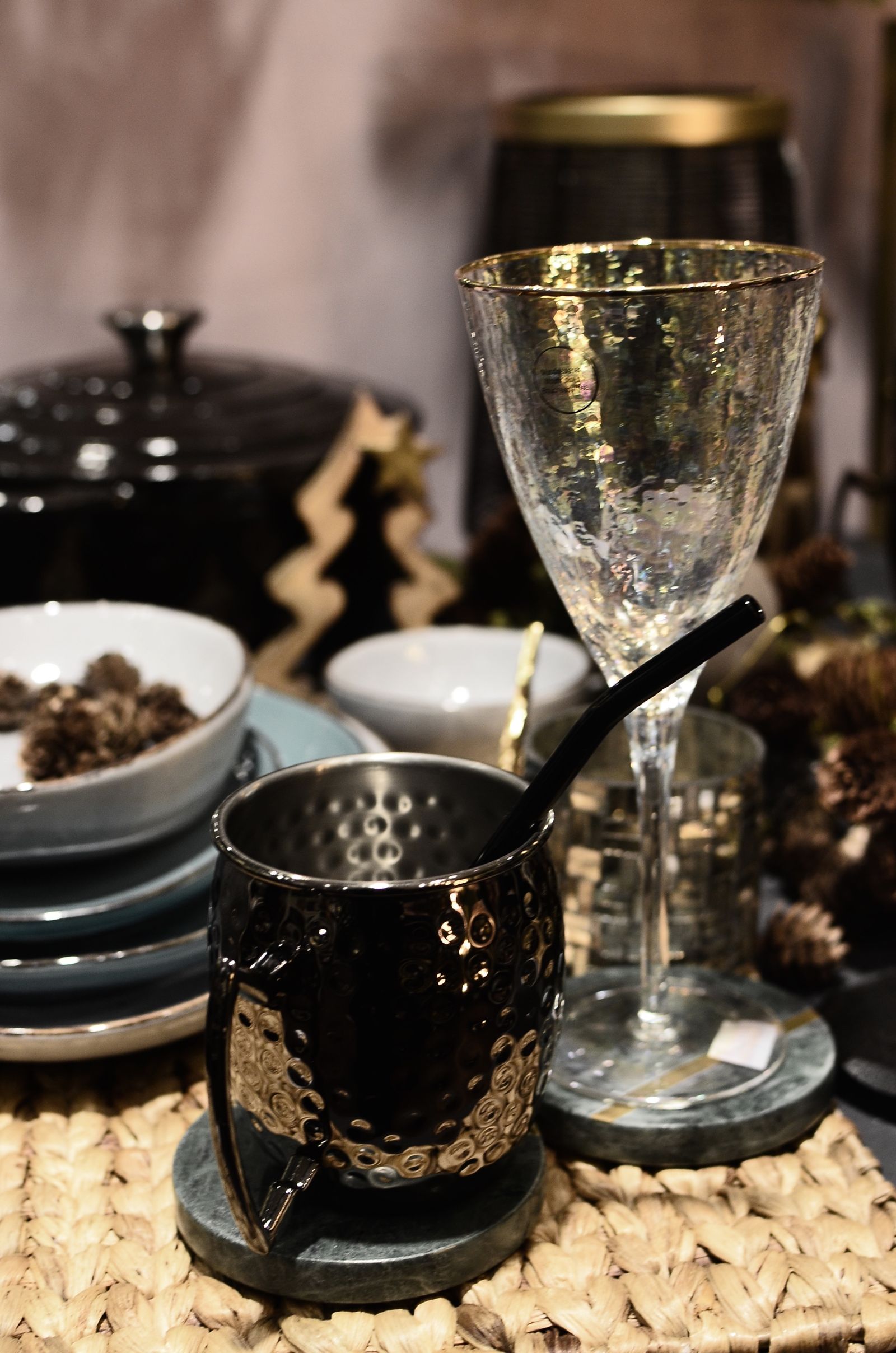 Metal pitcher, glassware, neutral dishes, and pine cones arranged on a holiday table.