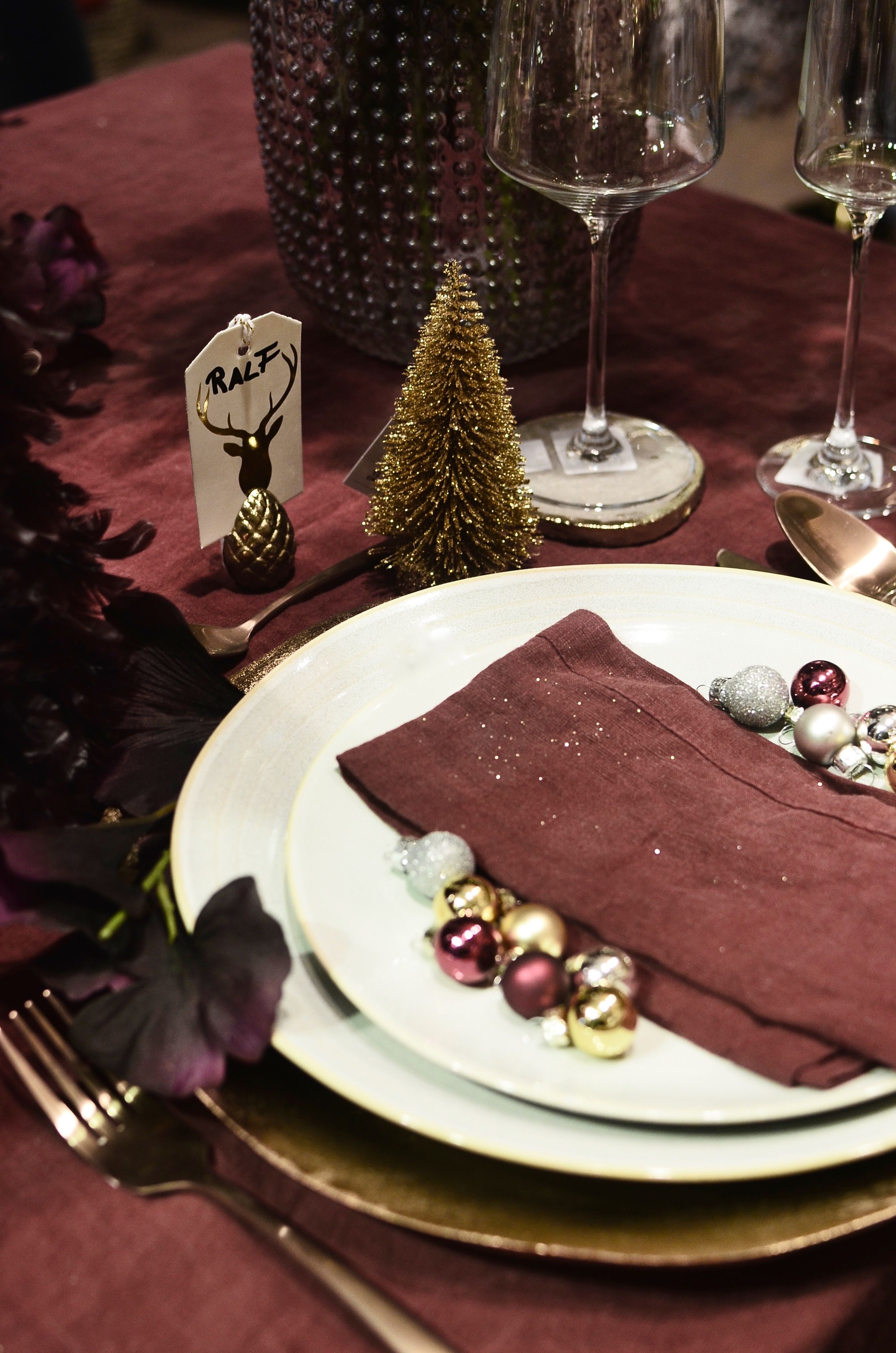 Table setting with dishware and fabric napkin between baubles near decorative Christmas tree in restaurant
