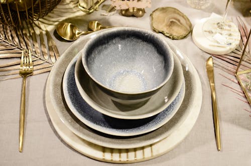 High angle of table setting with ceramic bowls and plates between cutlery on decorative sprigs