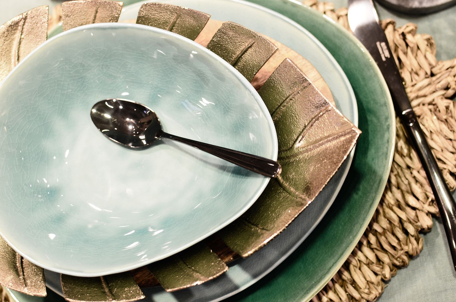 From above of served table with ceramic bowl and plates with spoon and knife on straw mat in restaurant