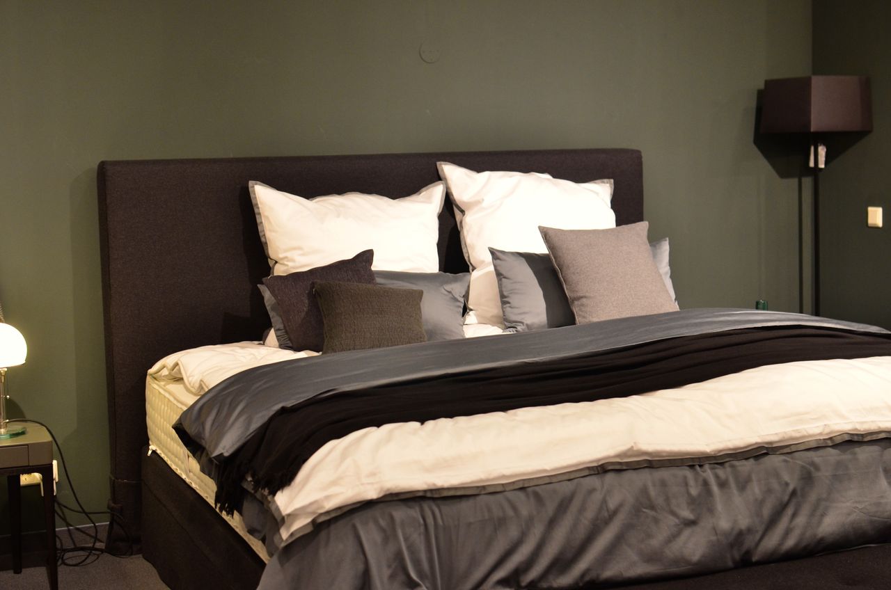 Bed styled in black and white with a white duvet, black throw layers, gray and white pillows and a tall black headboard