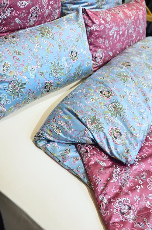 From above of assorted decorative pink and blue pillows near blanket on soft bed