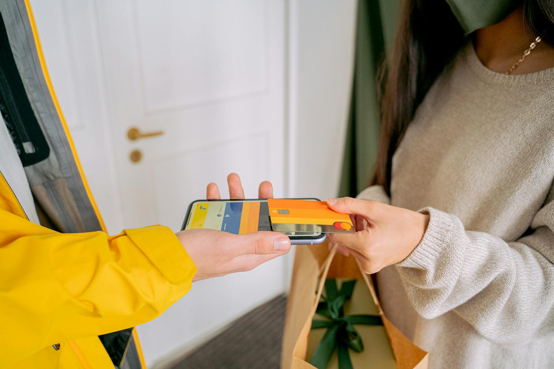 A Person in Knitted Sweater Holding a Credit Card while Putting on Top of the Phone