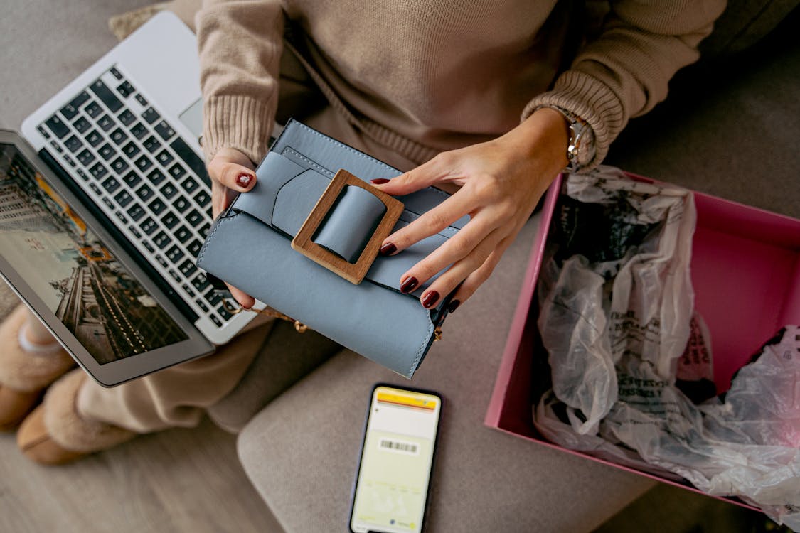 Free Woman Sitting on a Couch with a Laptop on Her Lap and Holding a New Purchase Stock Photo