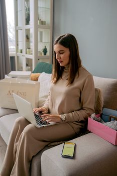 Young woman using laptop for remote work at home, seated on a comfortable couch.
