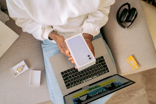 Free Person unboxing a new smartphone while sitting with a laptop, ready for online shopping on a cozy sofa. Stock Photo
