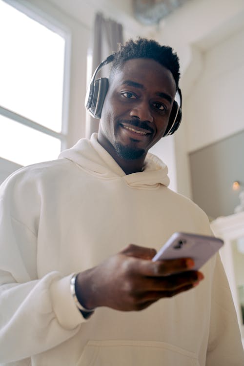 Young Man in Headphones Holding a Smartphone and Smiling