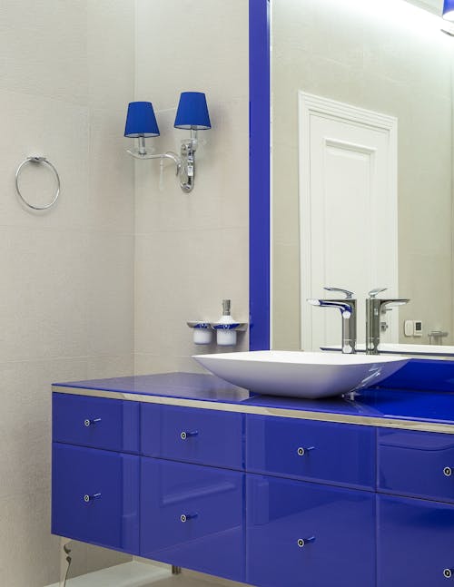 Interior of modern bathroom with blue cabinet with mirror and vessel sink and sconce on wall