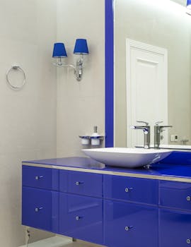 Interior of modern bathroom with blue cabinet with mirror and vessel sink and sconce on wall