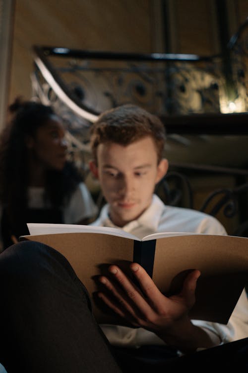 Man in White Long Sleeve Shirt Sitting while Reading a Book