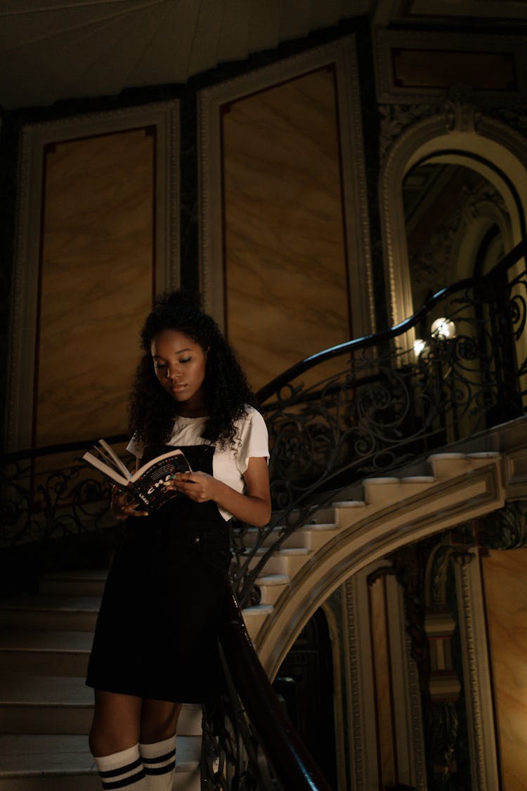 Woman Standing On The Stairs Reading A Book