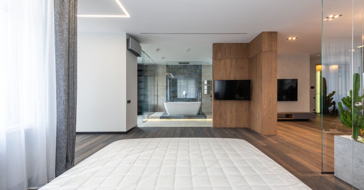 Interior of modern spacious apartment with wooden floor glass walls and bedroom looking into bathroom