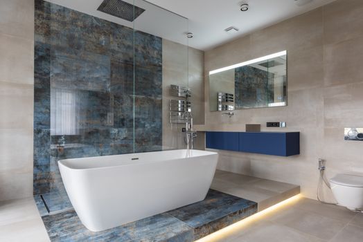 Stylish interior of modern bathroom with tiled walls and floor freestanding bath tub blue cabinet with sink