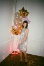 Young dreamy female in elegant apparel with assorted balloons looking down on floor in building