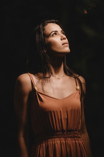 Young contemplative ethnic female with dark hair in elegant wear with pendant looking up in twilight