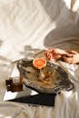 From above of crop anonymous female resting on crumpled bed sheet with ripe orange and alcoholic drink in glass on tray