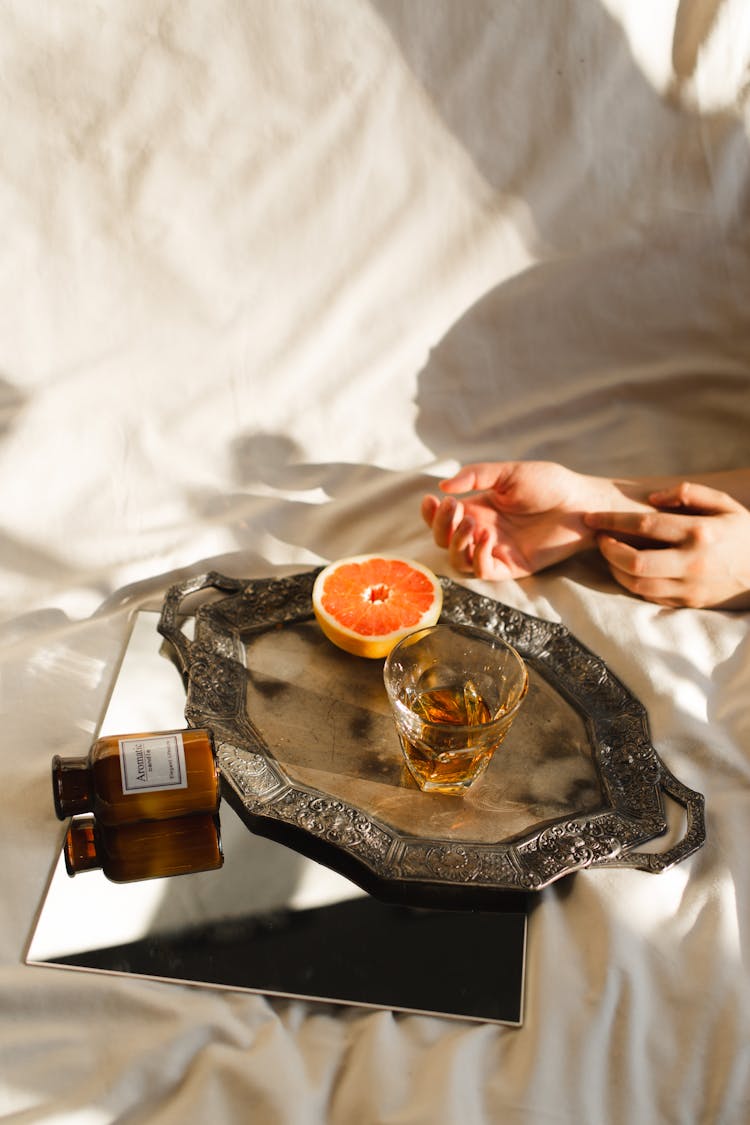 Crop Woman On Bed With Cut Orange And Brandy Indoors