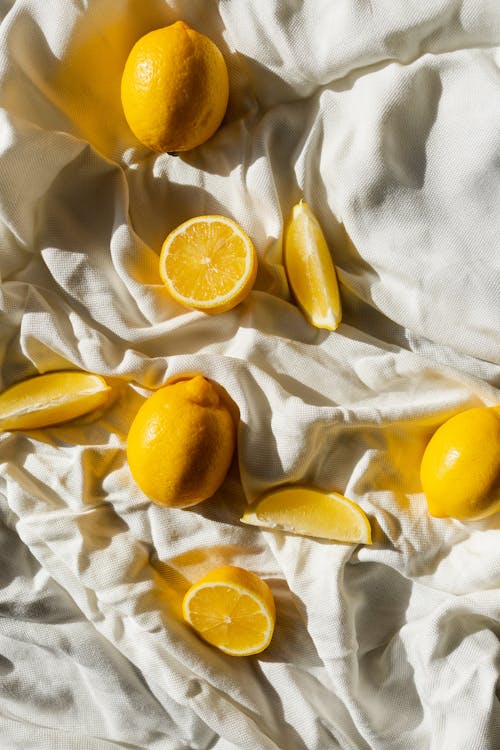From above of bright cut and whole juicy lemons on creased bed sheet in house in sunlight