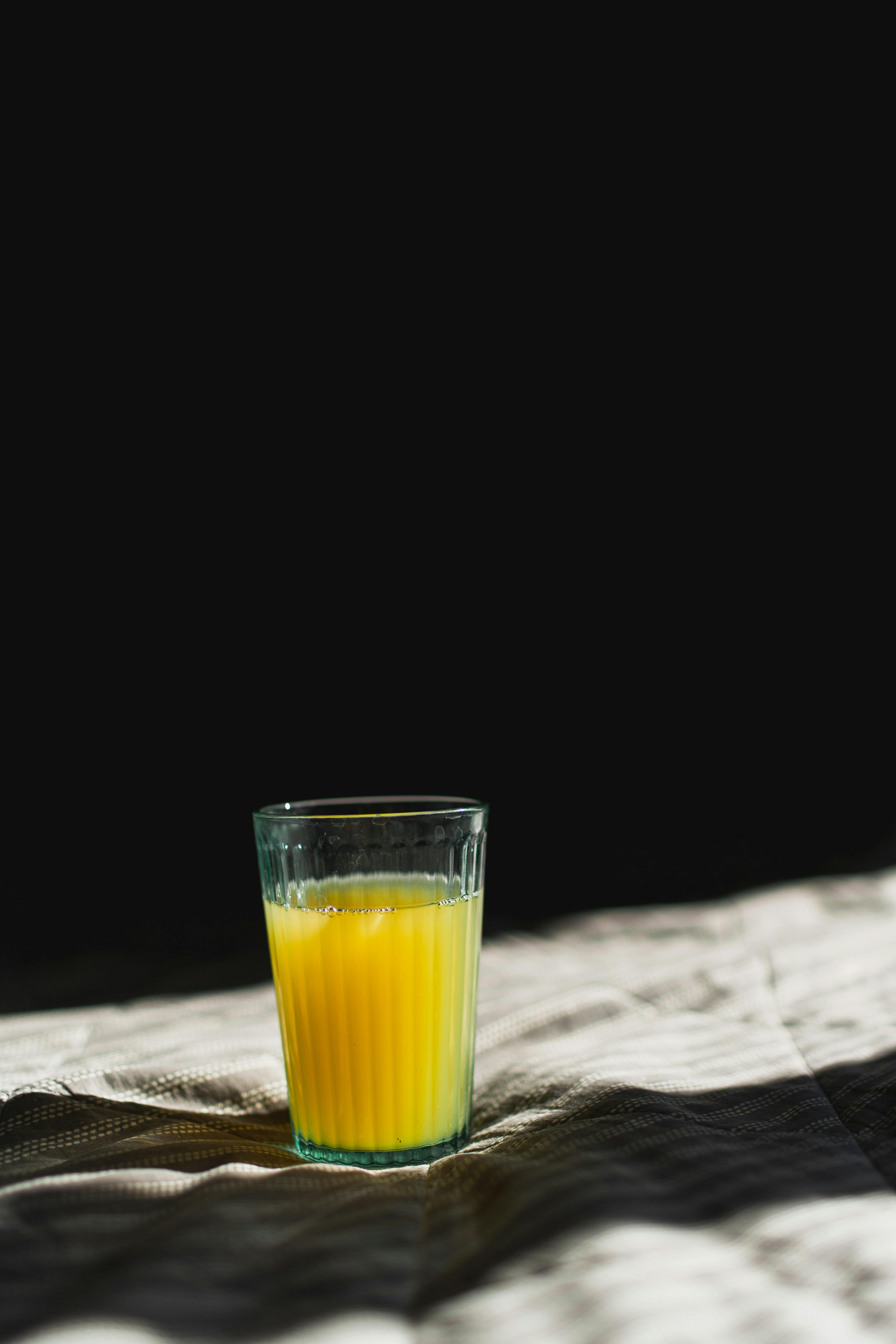 Transparent glass with bright citrus fruit juice on textile with shade in sunlight on black background