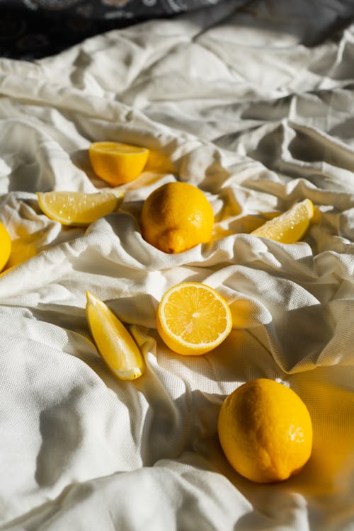 Cut and whole colorful juicy lemons with yellow peel on crumpled bed sheet at home
