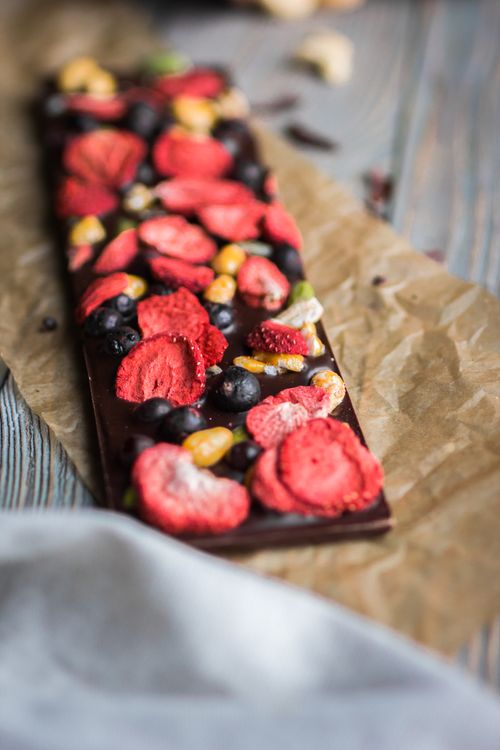 Free Artistic chocolate bar topped with dried berries and nuts on parchment paper. Stock Photo