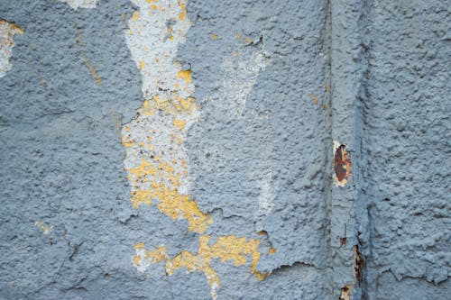 Textured background of weathered old cement building wall with cracked peeled gray paint