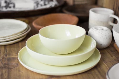 Set of stylish light ceramic crockery including bowls tea cups and plates placed on wooden table