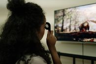 A woman with curly hair using a remote control to watch a nature documentary on a flat-screen TV indoors.