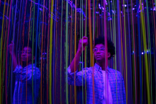 A young person interacts with colorful neon strings in a reflective art installation.
