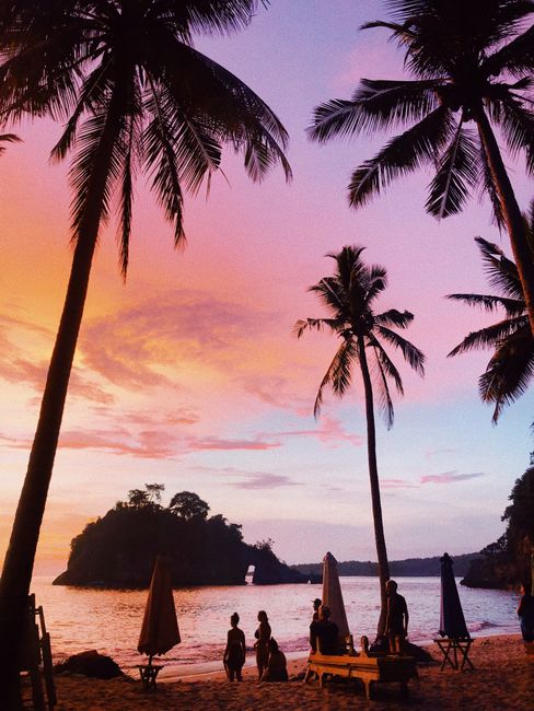 A breathtaking sunset in Bali with silhouetted palm trees and people on the beach, capturing tropical paradise bliss.